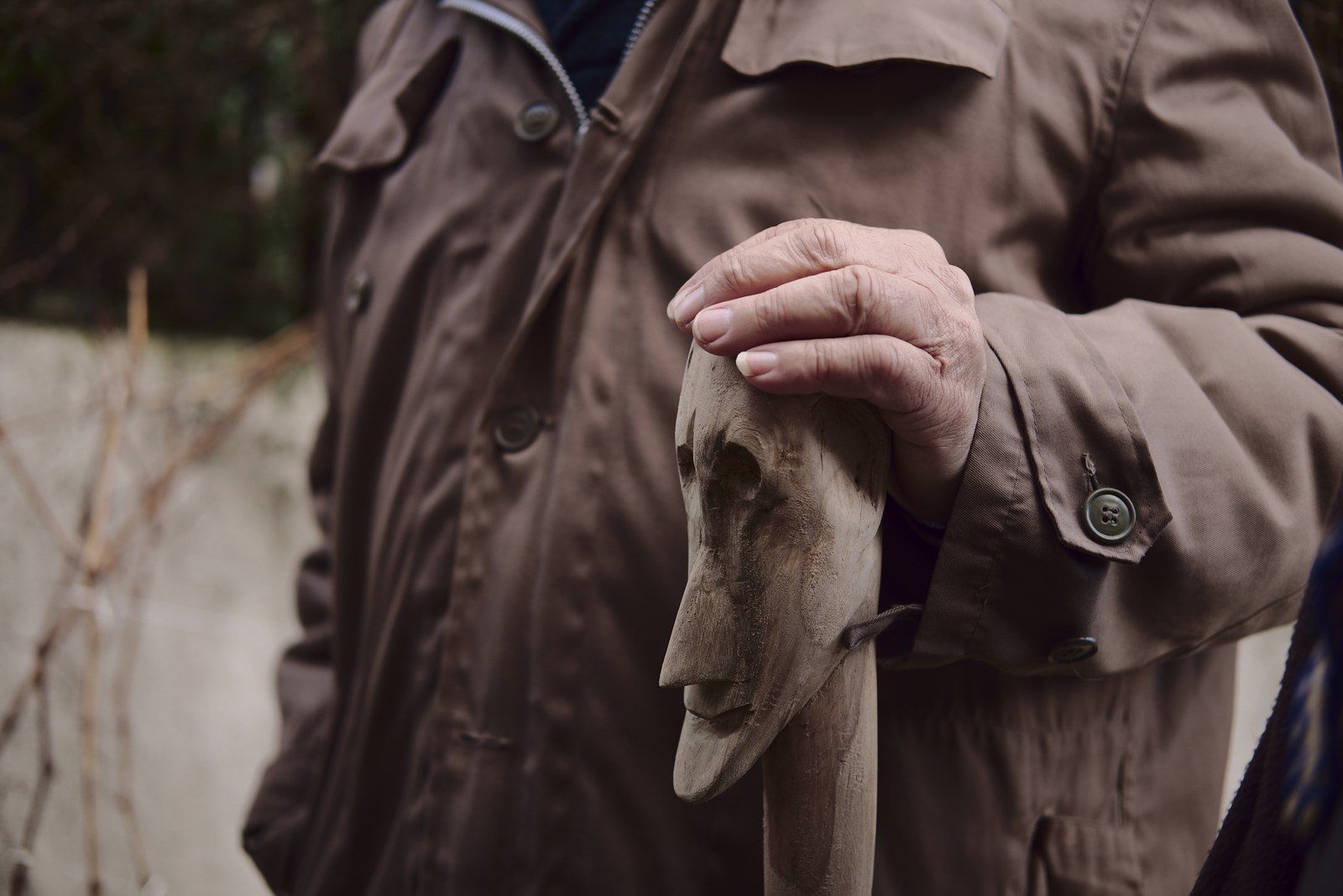 Elder man holding a cane with a carved mask in it.